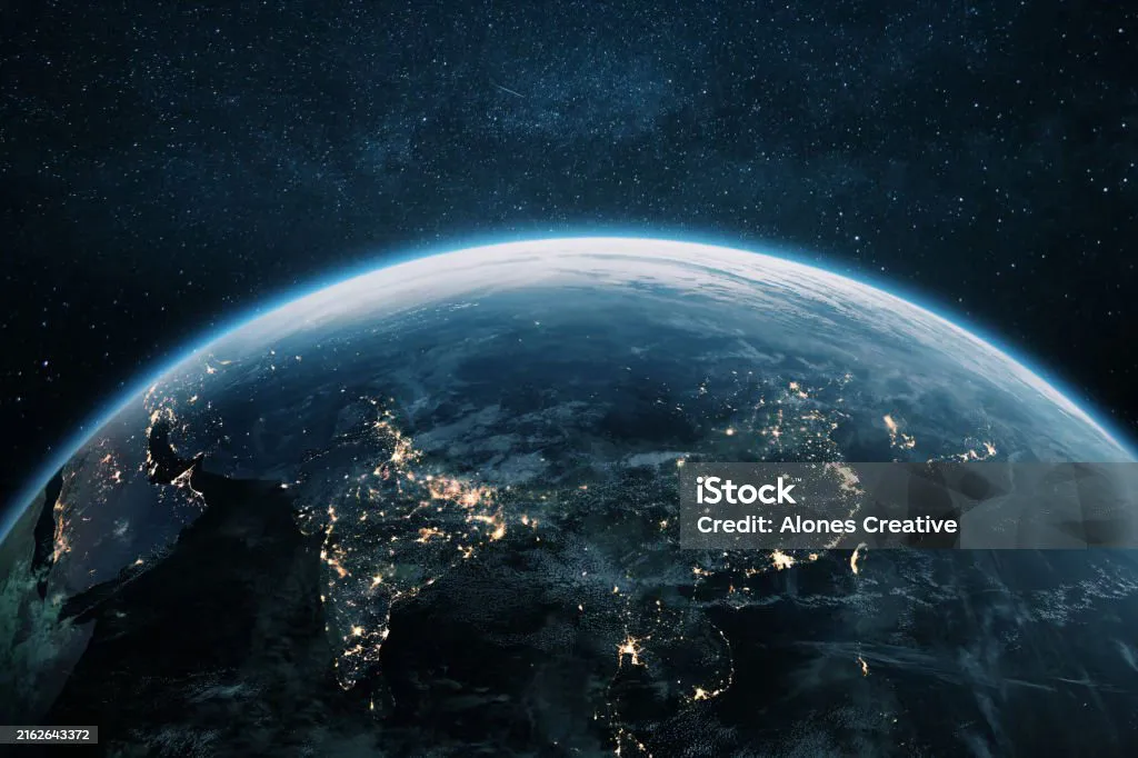 Nighttime view of Earth from space showing illuminated cities across Asia under a starry sky.