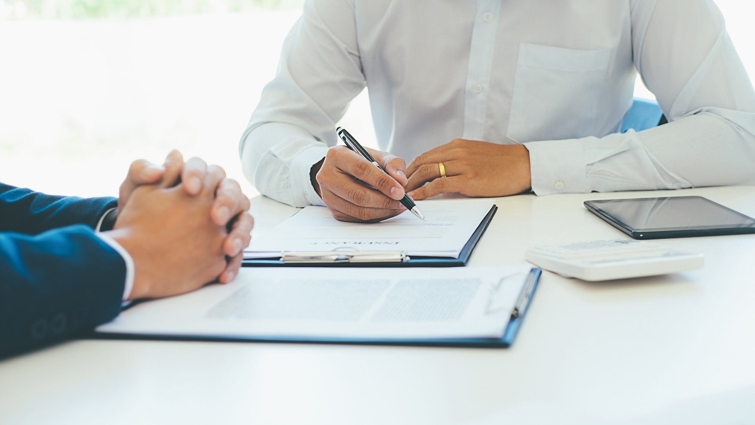 Zwei Personen bei Vertragsunterzeichnung, eine Person unterschreibt ein Dokument mit einem Stift.