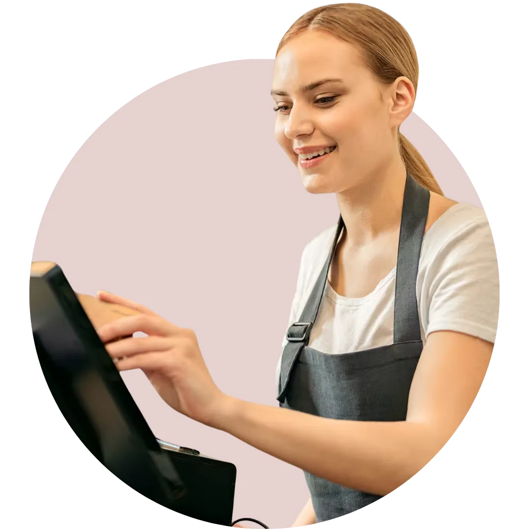 A friendly, smiling young female retail professional wearing a dark apron, operating a digital point-of-sale (POS) tablet system against a clean, modern background.