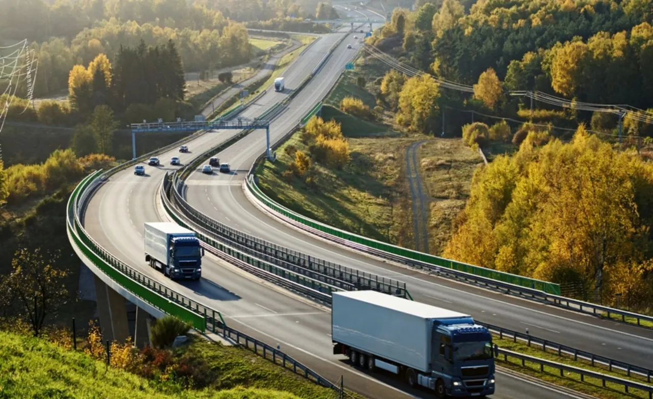 Two white trucks driving on a modern highway surrounded by autumn forest, symbolizing efficient logistics and transport.