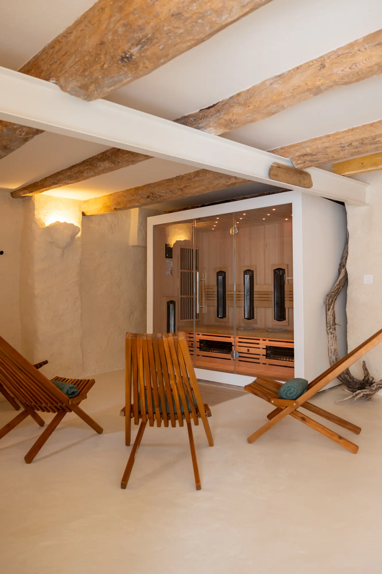 Espace bien-être à Casa Prana avec une cabine de sauna infrarouge en bois clair, entourée de chaises longues en bois, sous un plafond à poutres apparentes et un éclairage tamisé.