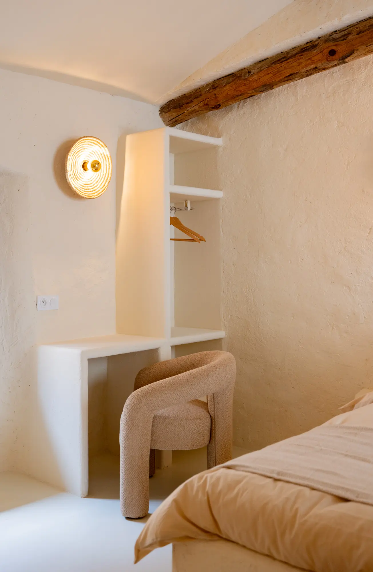 Coin bureau minimaliste dans une chambre à l’esthétique douce et naturelle, avec une chaise en tissu beige, une niche murale intégrée et des poutres en bois apparentes.