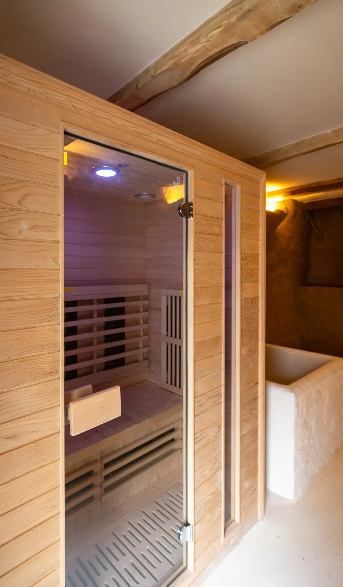 Cabine de sauna en bois clair dans un espace bien-être à La Garde, avec éclairage tamisé et murs texturés, évoquant une atmosphère chaleureuse et apaisante.