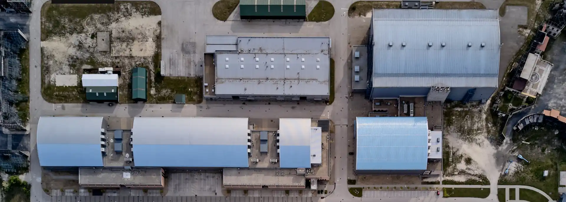 Aerial view of an industrial complex with multiple large white and blue-roofed buildings and surrounding parking lots.