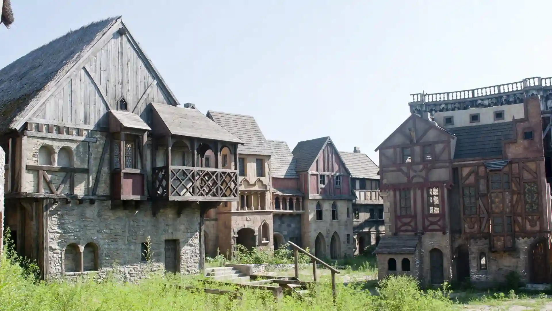 Row of medieval-style stone and timber buildings with steep roofs and a balcony under a clear sky.