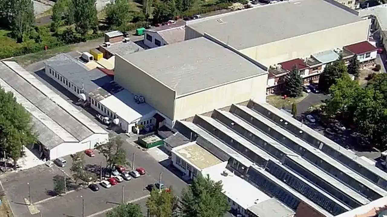 Aerial view of an industrial complex with multiple warehouse buildings, parking areas, and surrounding trees.