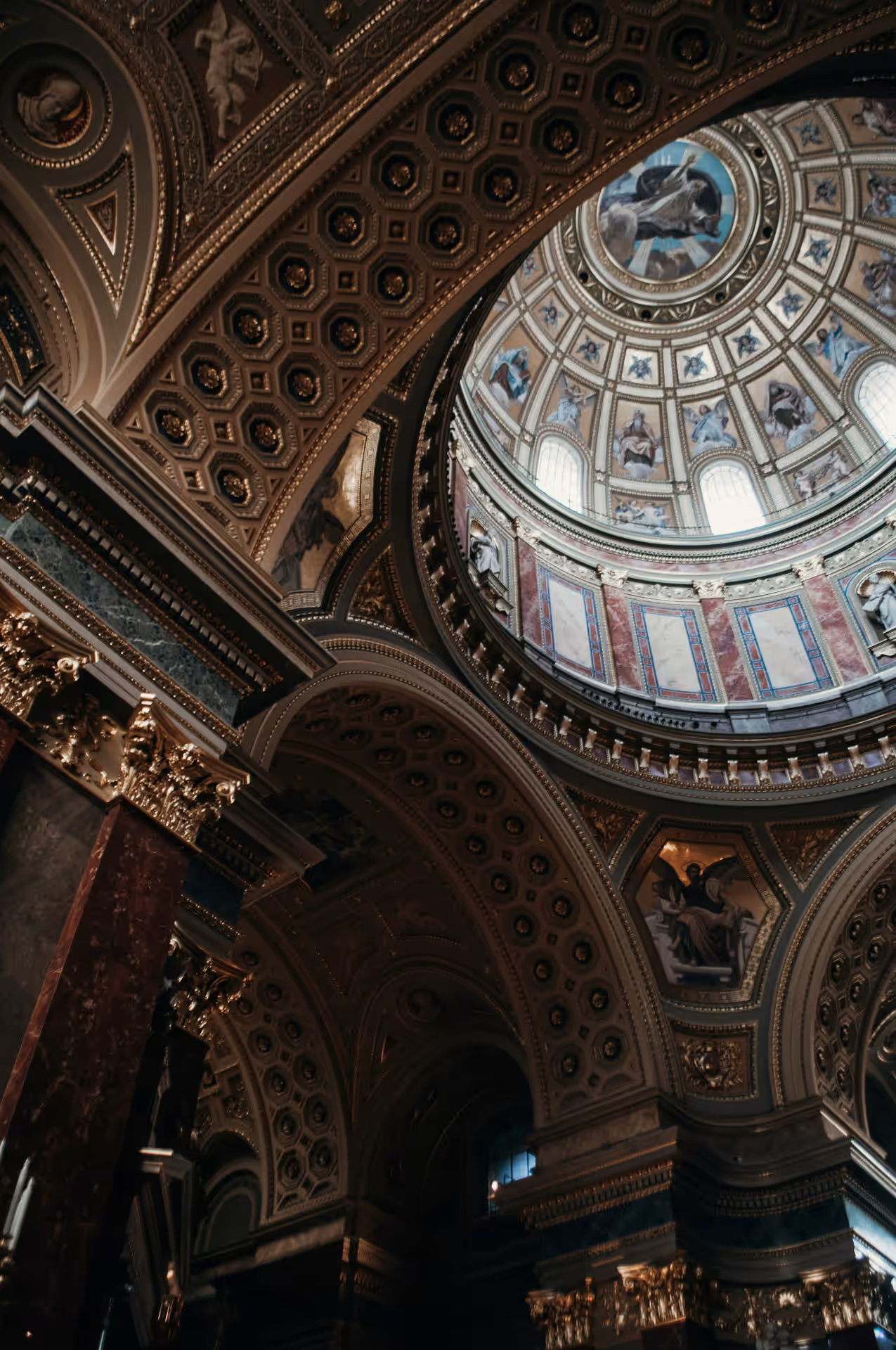 Ornate dome ceiling with classical paintings and gold architectural details inside a grand historic building.