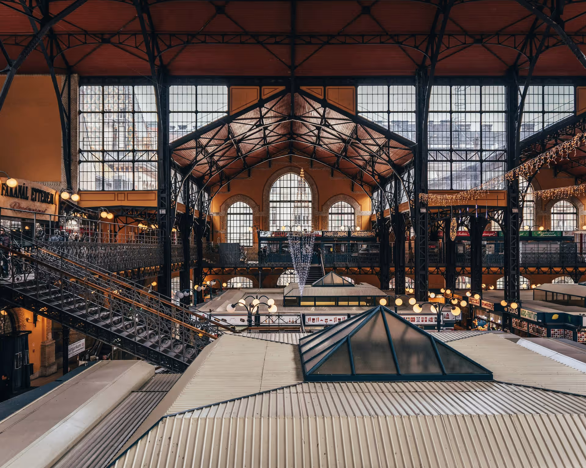 Interior of a large historic market hall with ornate ironwork, high windows, and multiple rooftops of stalls.