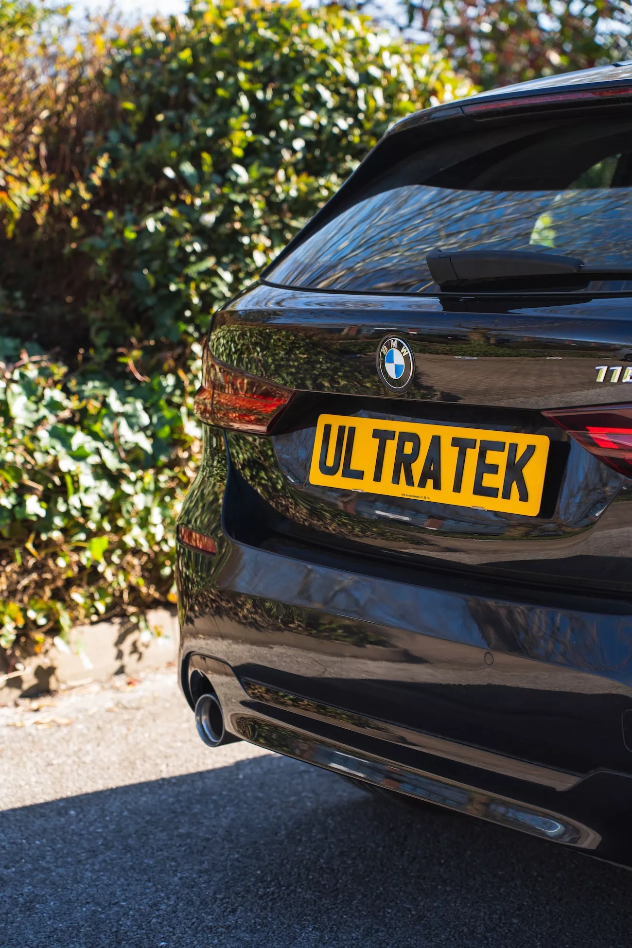 Yellow acrylic rear number plate showing a private "ULTRATEK" registration fitted to a black BMW