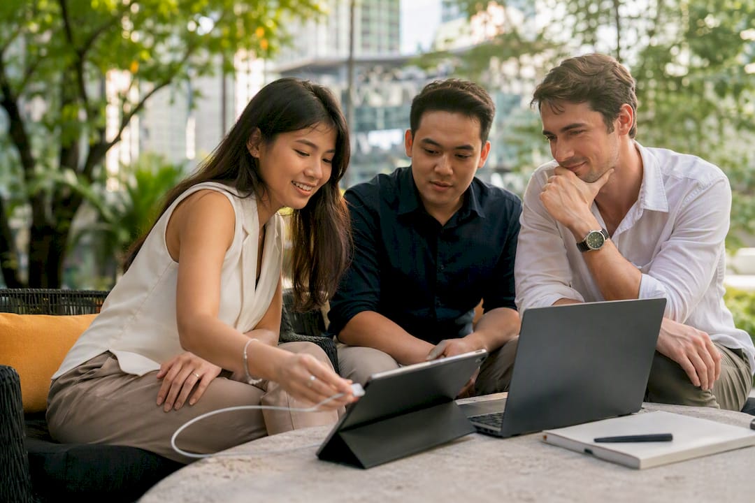 Three founders reviewing work on a tablet and laptop at an outdoor table in the city