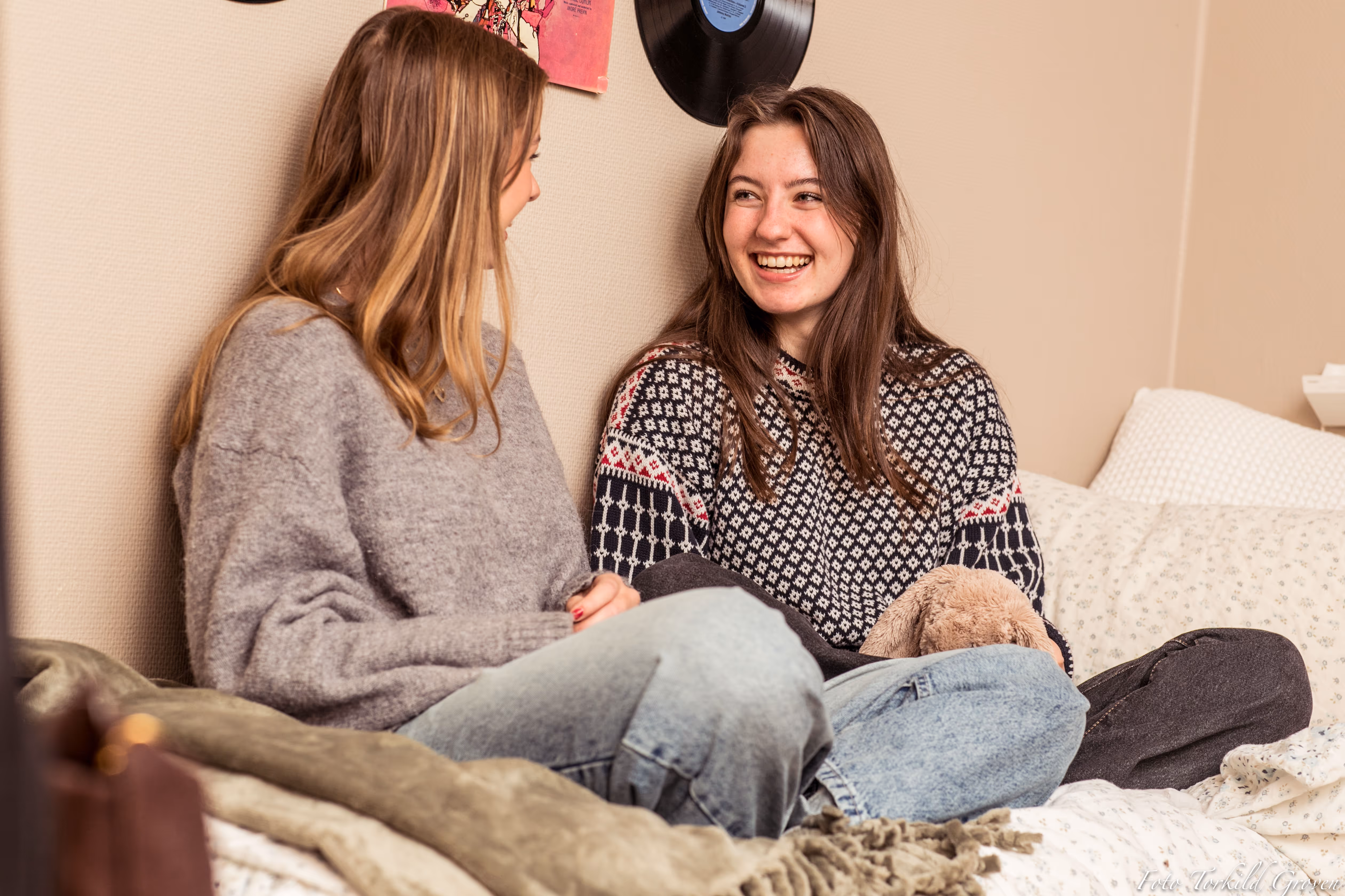 To elever sitter på sengen og ler sammen på et elevrom ved Karmøy Folkehøgskole, med vinylplater og plakater på veggen bak