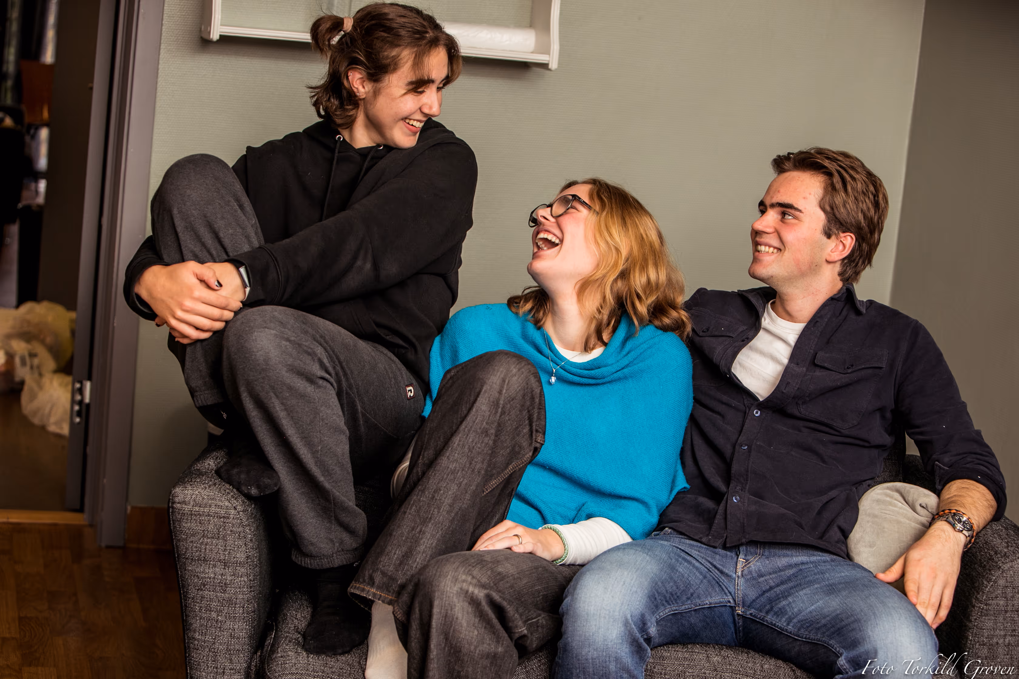 Tre elever ved Karmøy Folkehøgskole sitter i sofaen og ler sammen i en hyggelig stueatmosfære