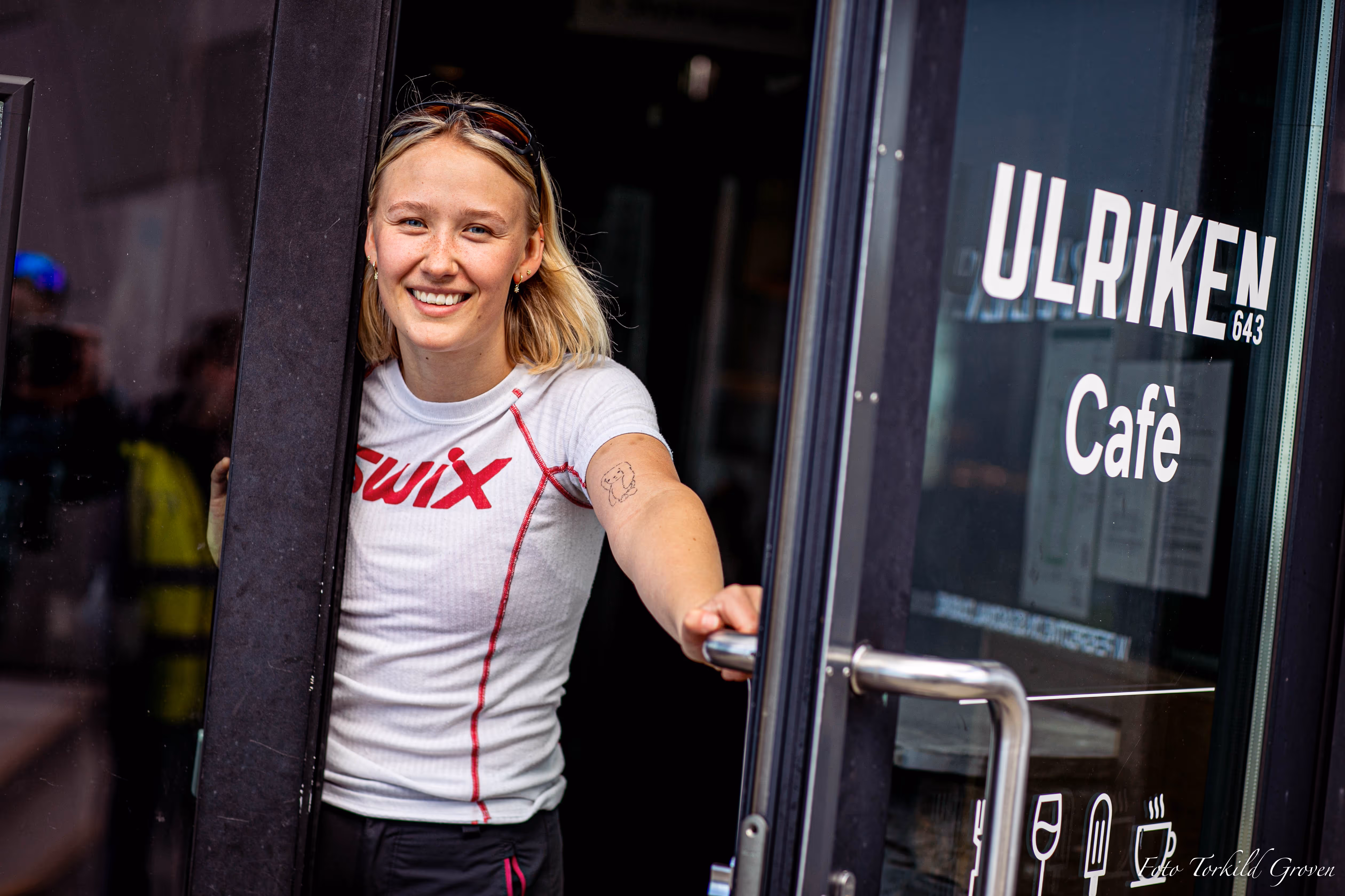 En elev fra Karmøy Folkehøgskole smiler i døra til Ulriken Café etter en tur, iført treningstøy fra Swix