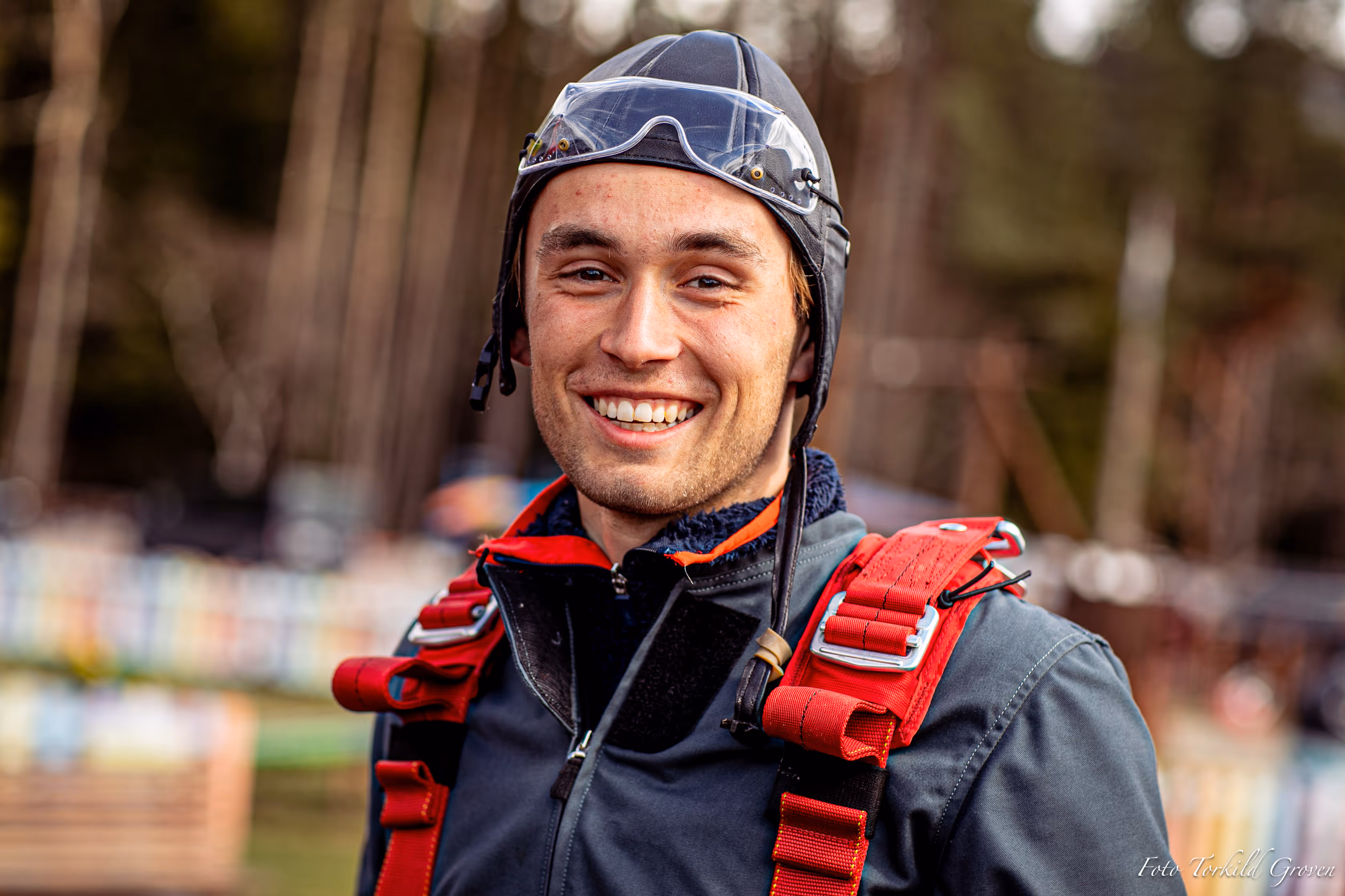 En elev ved Karmøy Folkehøgskole smiler mot kamera iført hjelm og sikkerhetssele før fallskjermhopp
