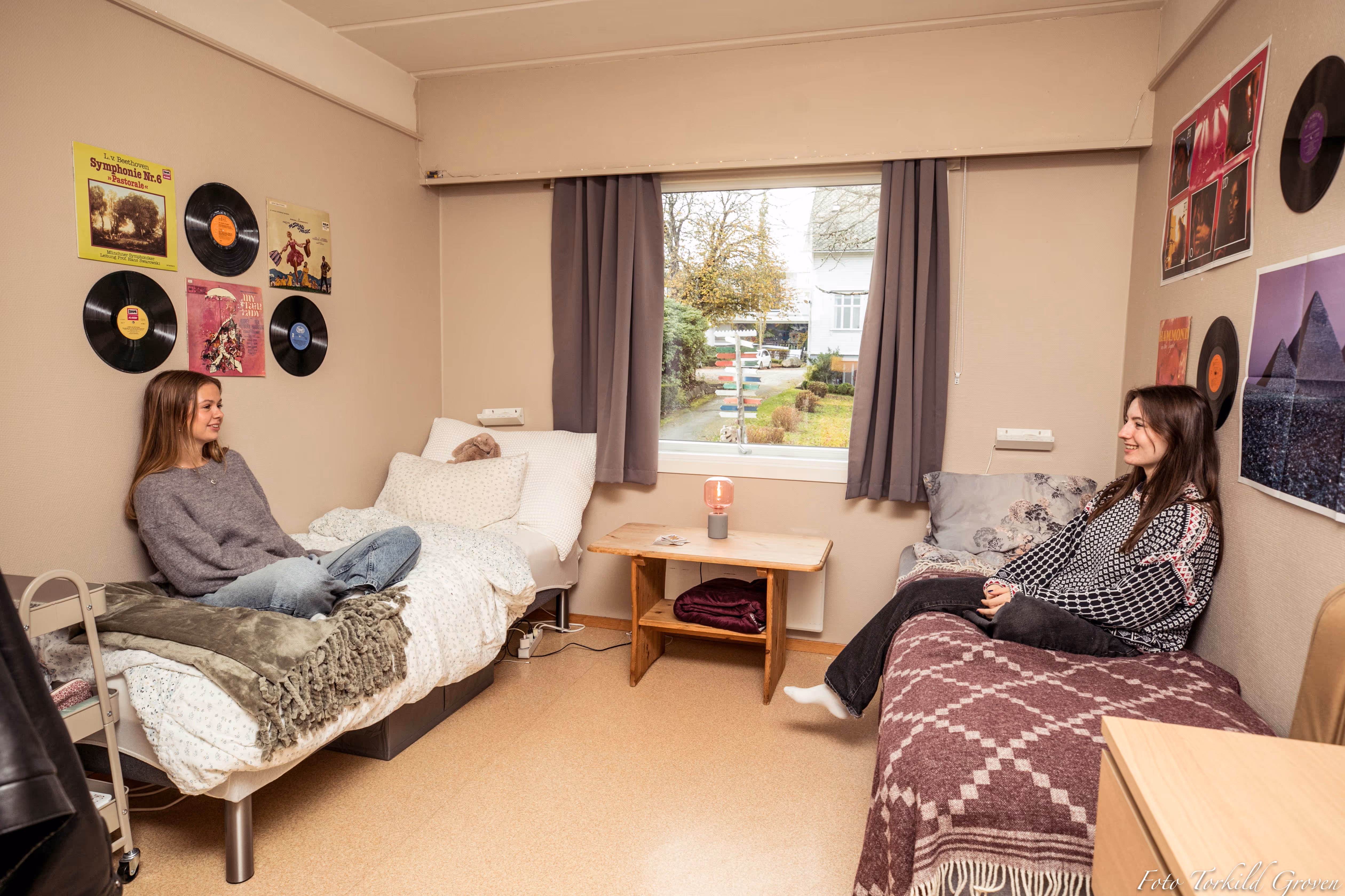 To elever slapper av og prater på internatrommet ved Karmøy Folkehøgskole med vindu mot skolens uteområde