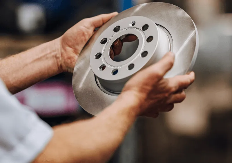 Person holding a new metallic car brake disc rotor with both hands.