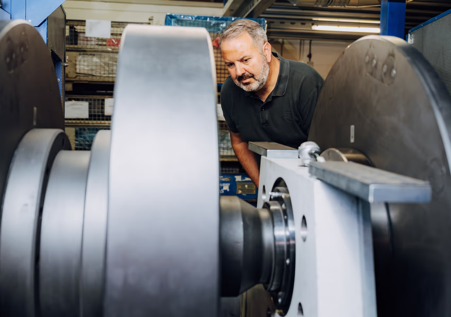 Man with gray beard inspecting large industrial machinery in a factory setting.
