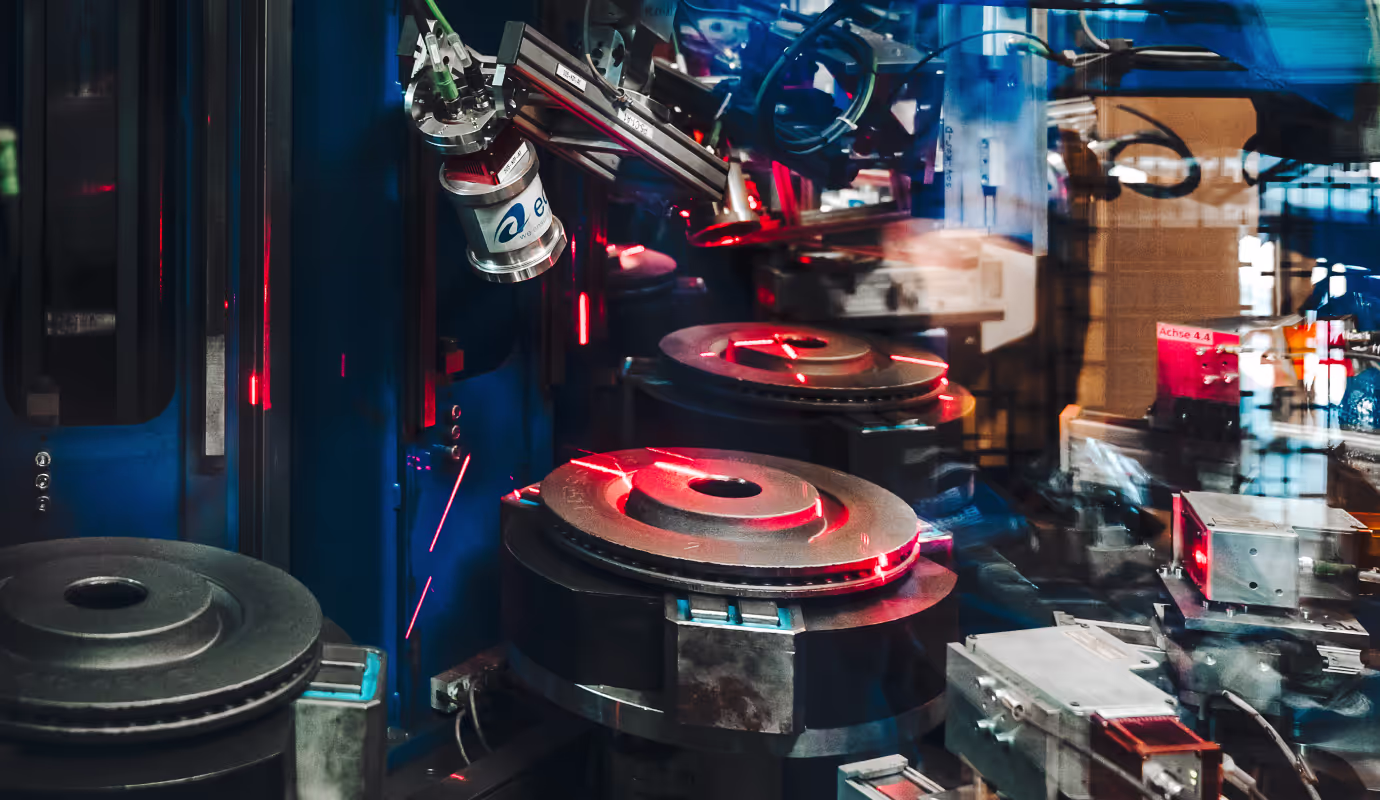 Automated machinery inspecting metal brake discs with red laser sensors in an industrial setting.