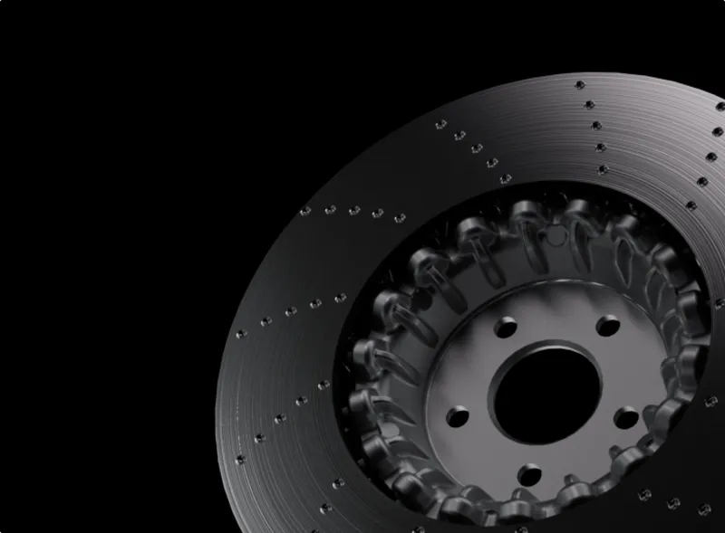 Close-up of a black drilled and slotted brake disc rotor on a black background.