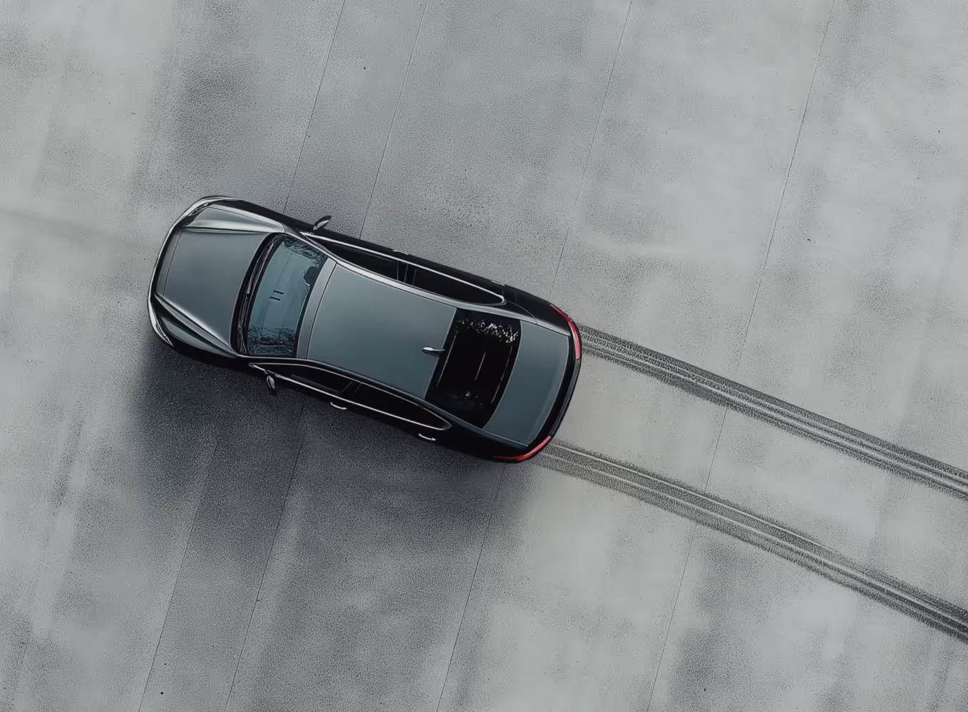 Top-down view of a black car on a concrete surface with tire skid marks behind it.
