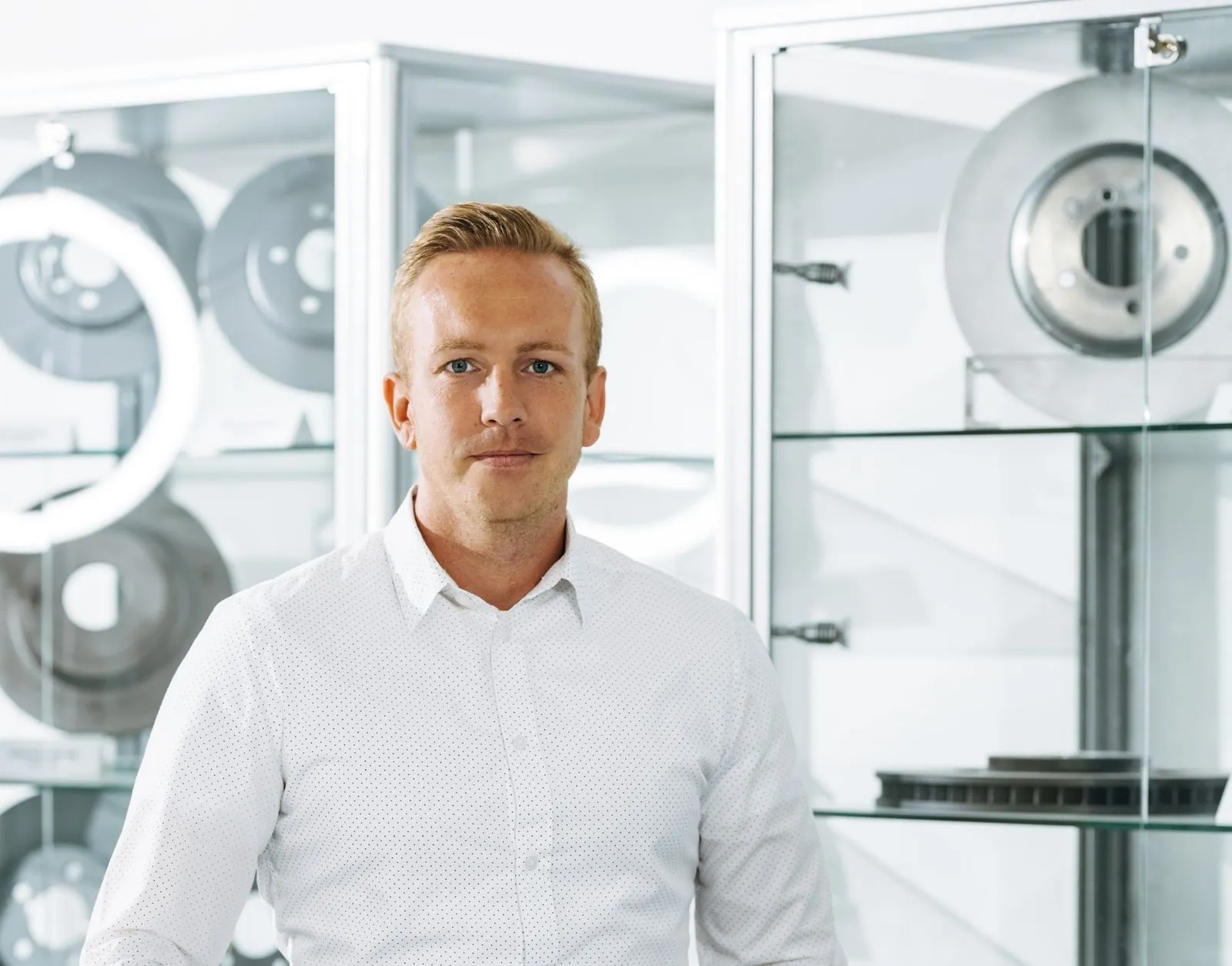 Man in a white button-up shirt standing in front of glass shelves with metal discs.