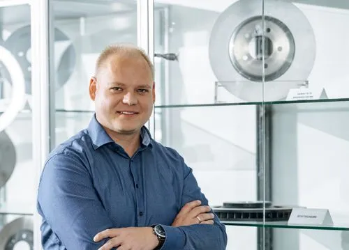 Smiling man with crossed arms standing in front of glass shelves displaying automotive parts.