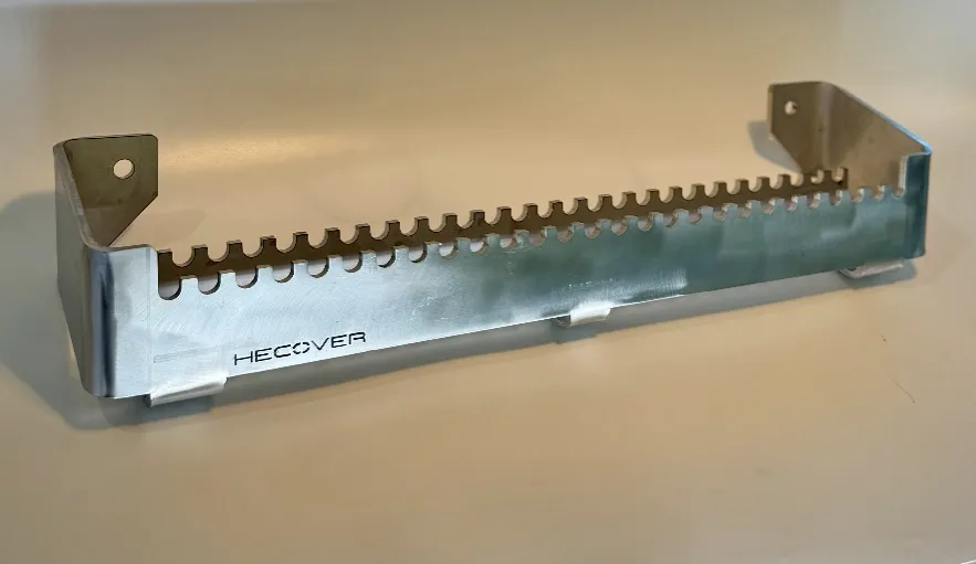 Metallinen ohjaamon sivuaskeleen kiinnitysteline, jossa on hammastettu yläreuna ja HECCOVER-logo.
