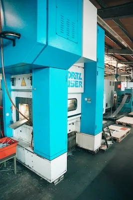 Blaues Industriemaschinen-Modell Dritz Buser in einer Fabrikhalle mit Förderbändern und Arbeitsbereich.