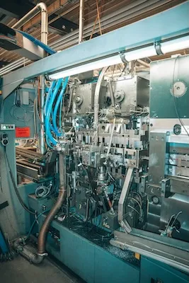 Industrielle Maschine mit Metallteilen, blauen Schläuchen und Steuerungskomponenten in einer Produktionsanlage.