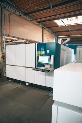 Industrielle Druckmaschine mit Touchscreen-Bedienfeld in einer Fertigungshalle.