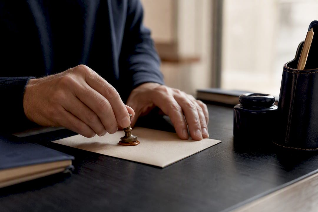 Des mains apposent un sceau sur des documents patrimoniaux posés sur le bureau.
