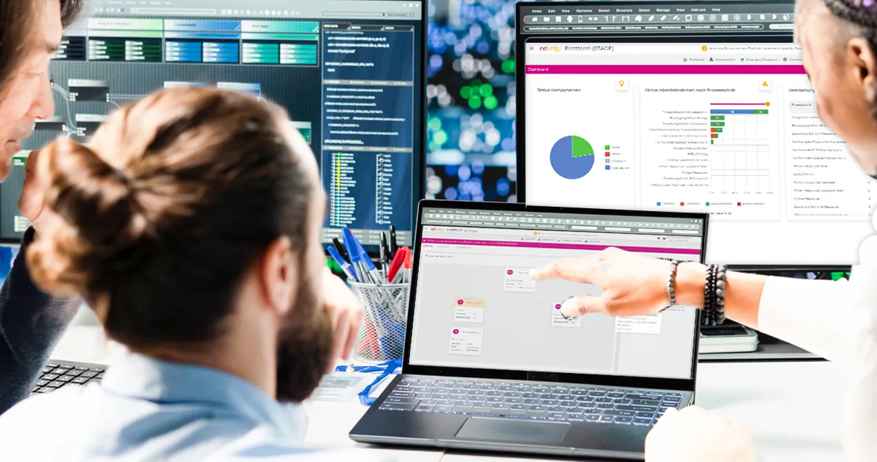 Drei Personen diskutieren über Diagramme und Daten auf drei Computerbildschirmen im Büro.