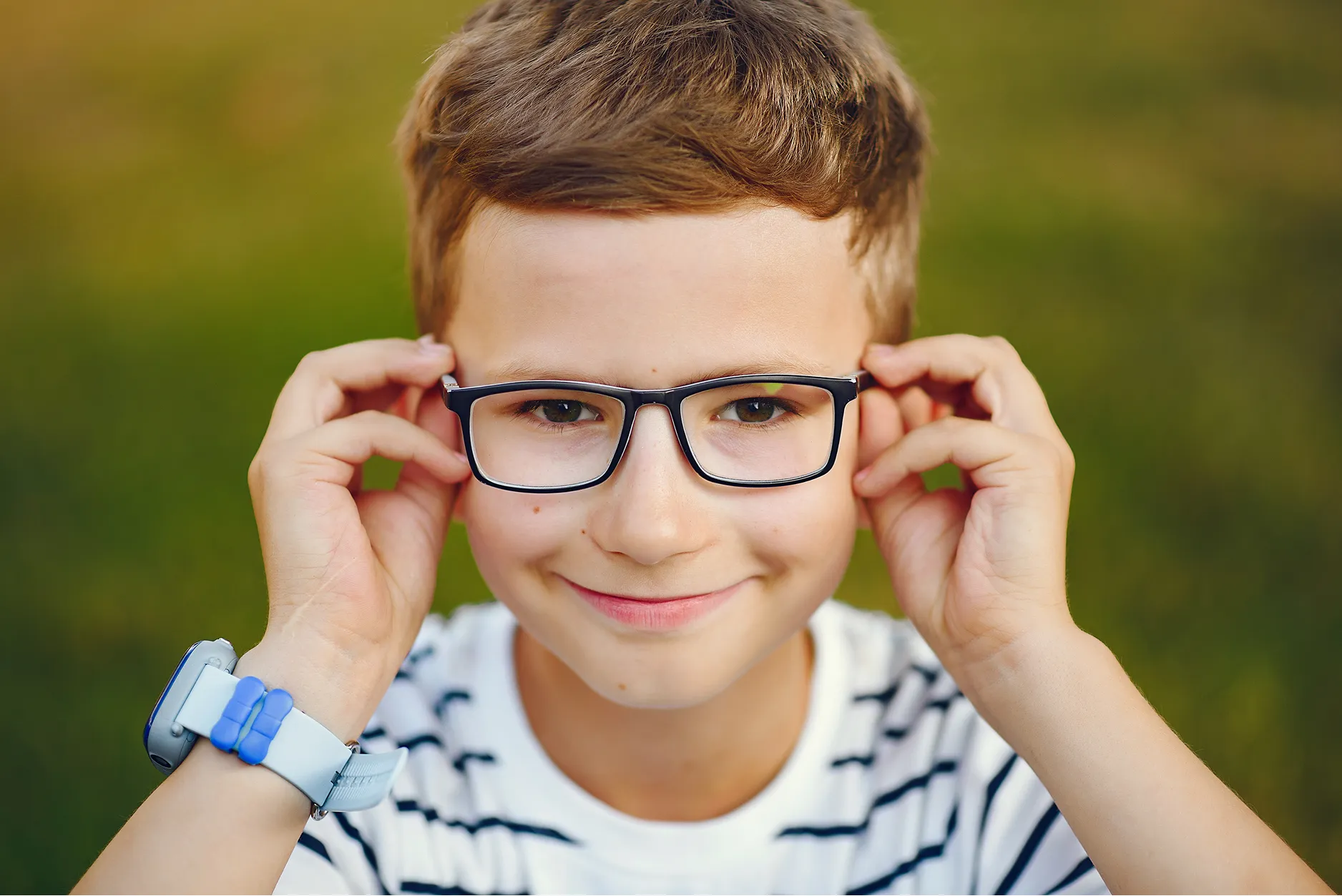 Young person adjusting glasses, smiling, wearing striped shirt and blue watch