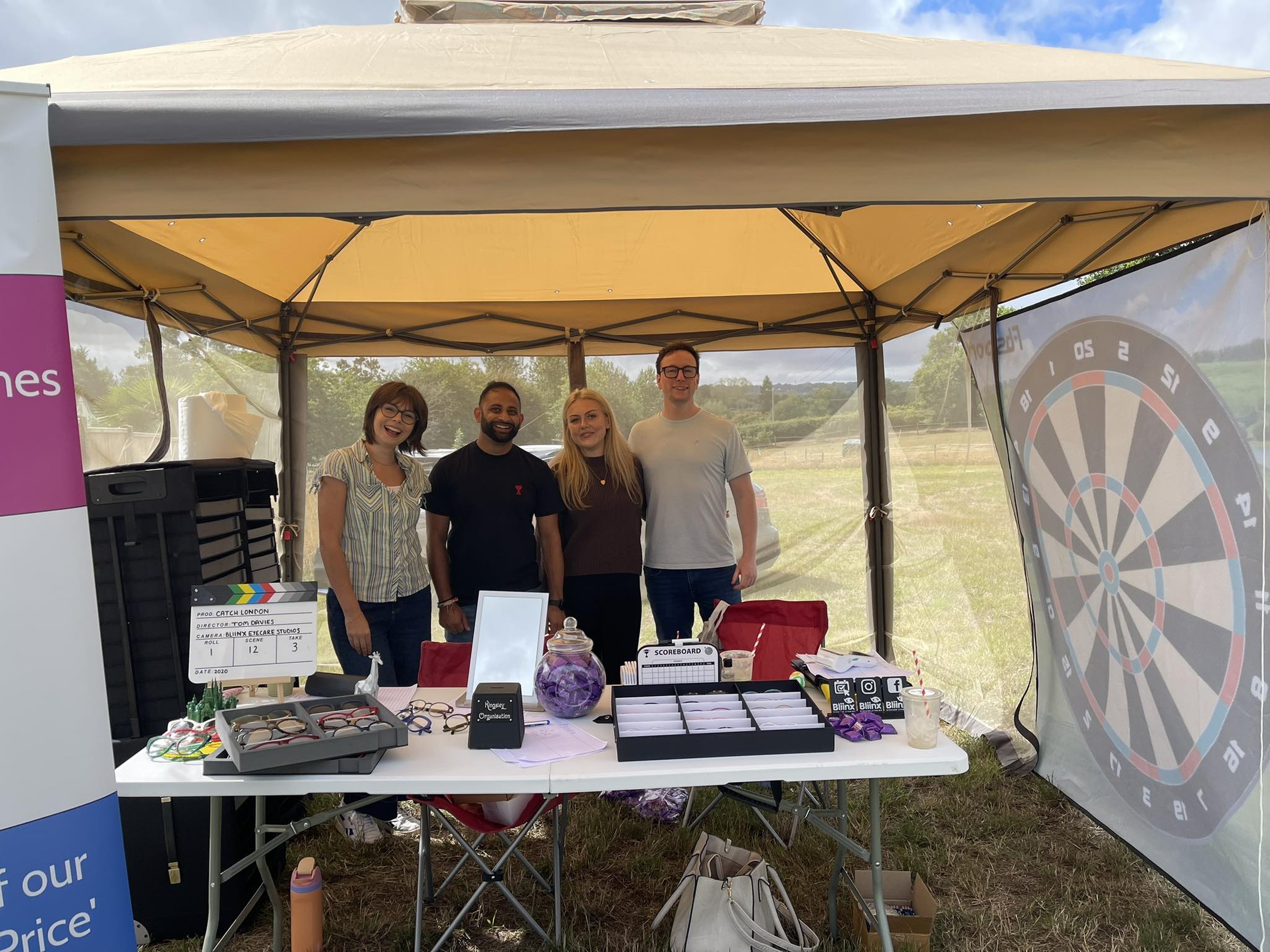 Team at outdoor event booth with dartboard, glasses, and promotional materials