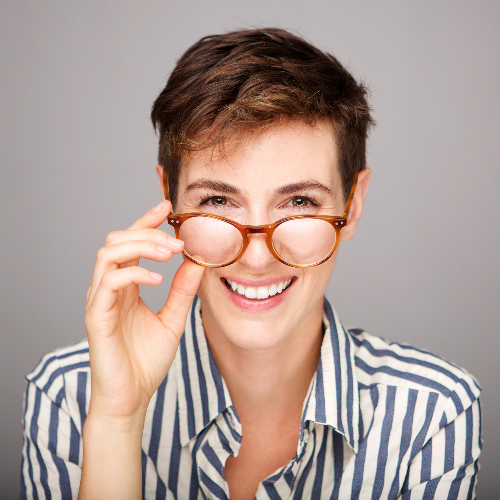 Smiling person with short hair adjusting amber glasses, wearing striped shirt