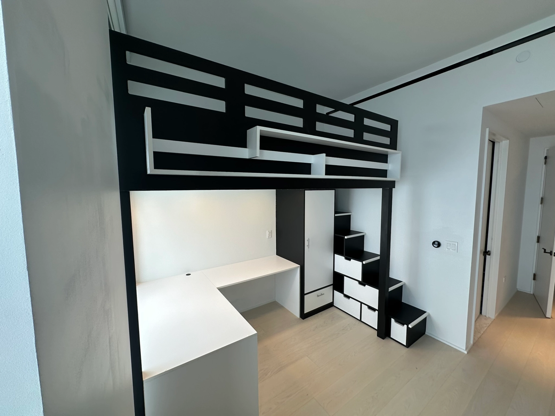 Modern black and white loft bed with built-in desk, storage stairs, and wardrobe in a minimalist room.