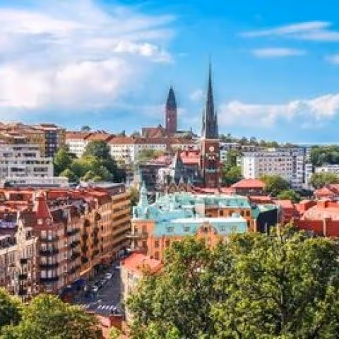 Gothenburg városképe zöld fákkal, vörös tetőjű épületekkel és két templomtoronnyal, tiszta kék ég alatt.