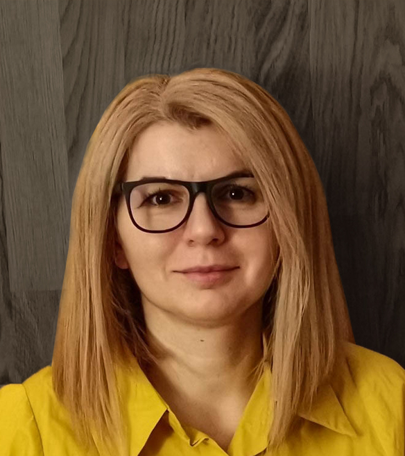 Szőkés szemüveges nő, sárga ingben egy fa hatású fal előtt