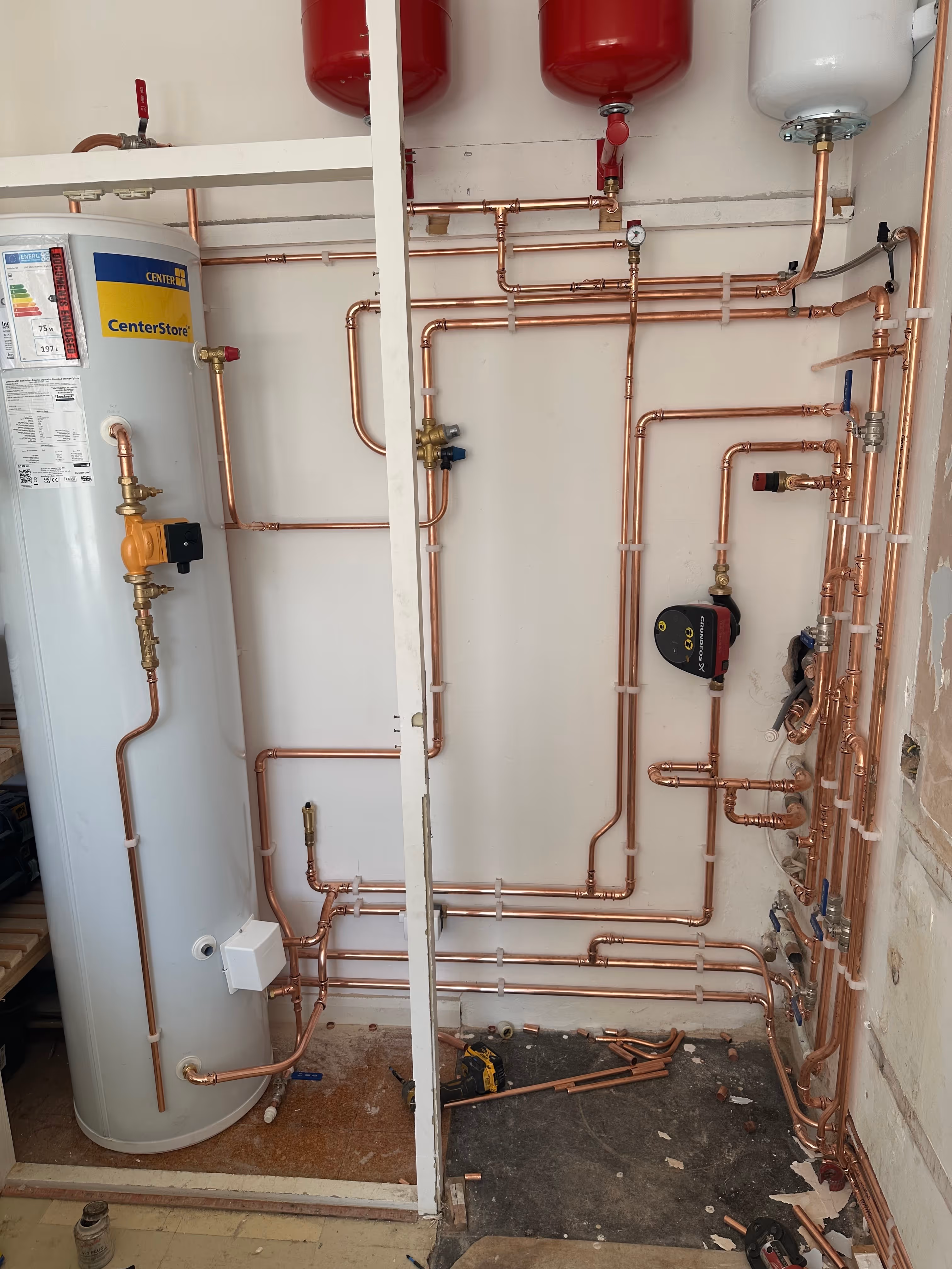 Indoor plumbing setup with a tall white water heater tank labelled CenterStore and multiple copper pipes connected to gauges and valves on a wall.