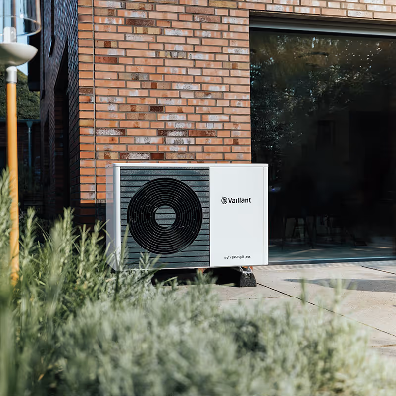 Vaillant heat pump unit installed outside a brick house near a patio door.