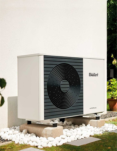 White and black Vaillant aroTHERM plus heat pump installed outdoors on concrete blocks surrounded by white pebbles.