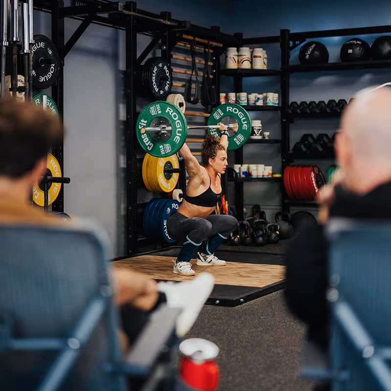 Female athlete performing a deep squat with a weighted barbell overhead.
