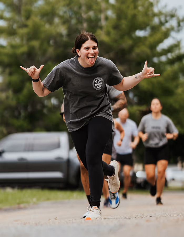 Young woman running outdoors with her tongue out and hands forming rock-on gestures.