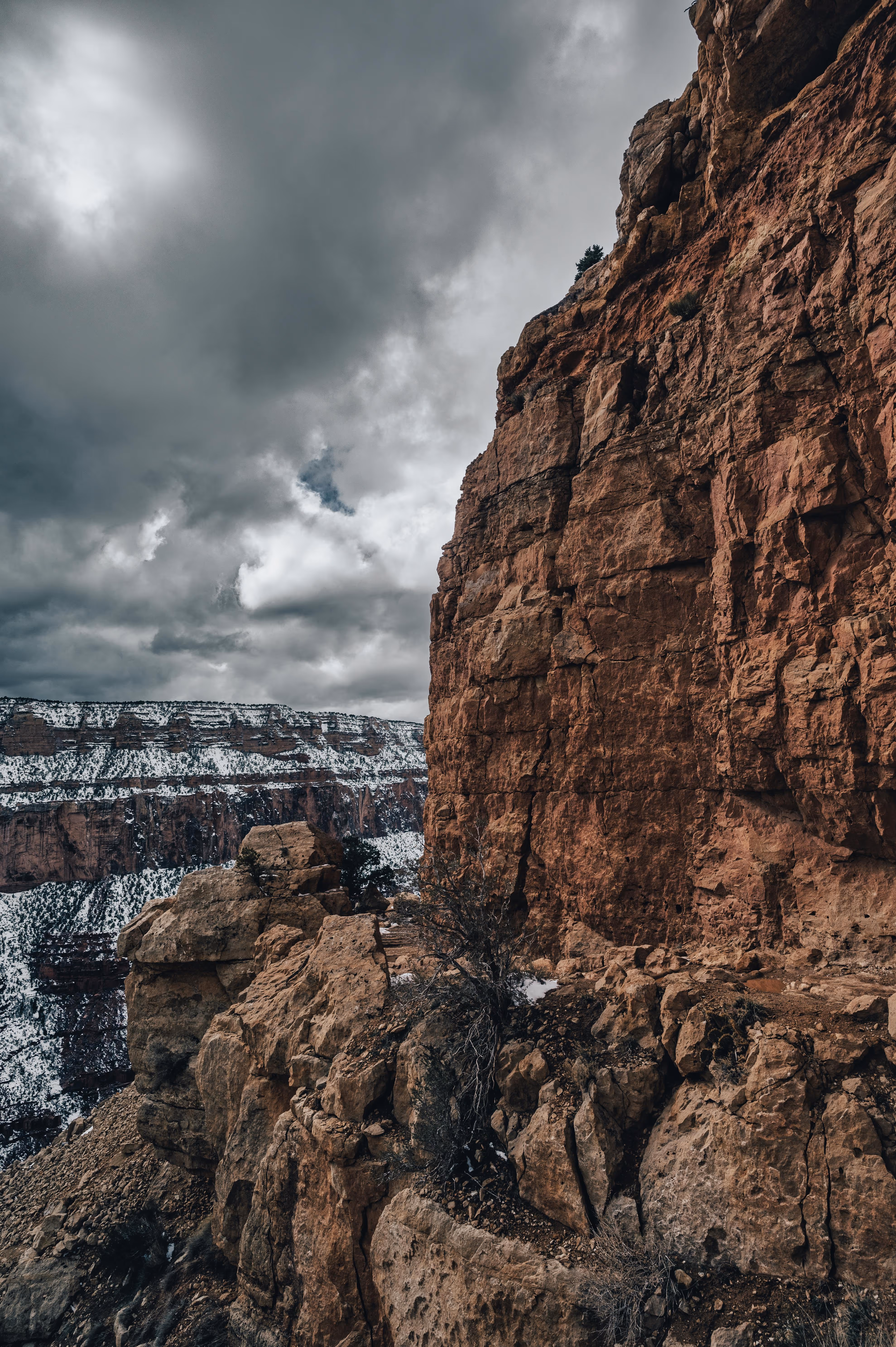 Grand Canyon cliff with patches of snow under a cloudy sky.
