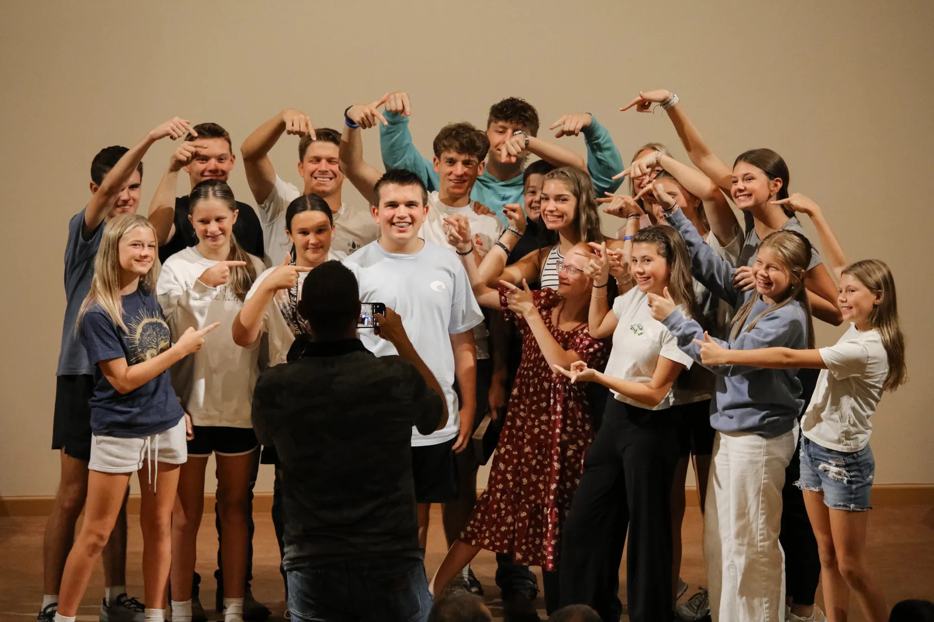 Group of smiling teenagers pointing at a teen who is being photographed.