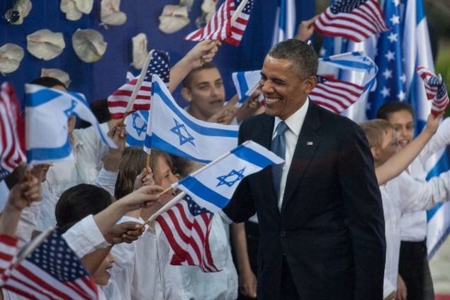 President Obama stands in front of American and Israeli flags.