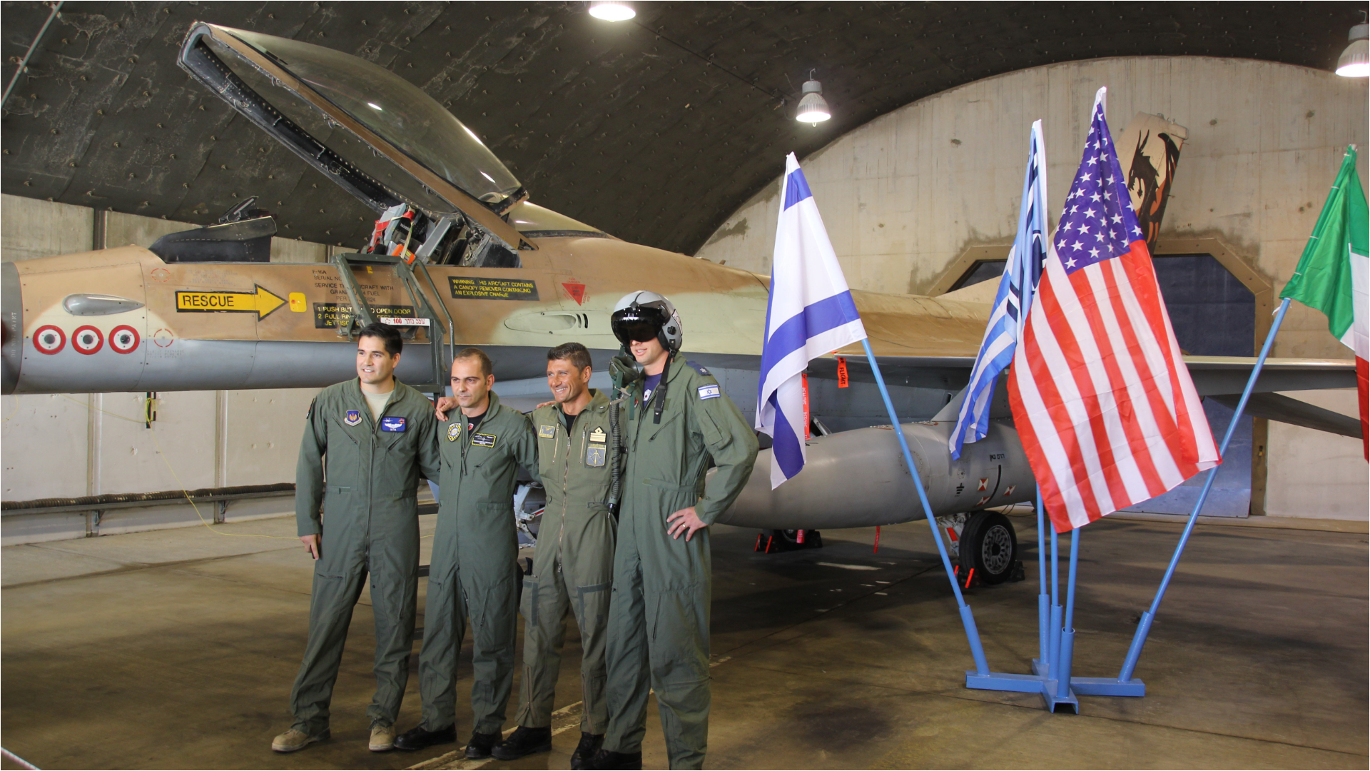 American servicemembers standing in front of a fighter jet and American and Israeli flags