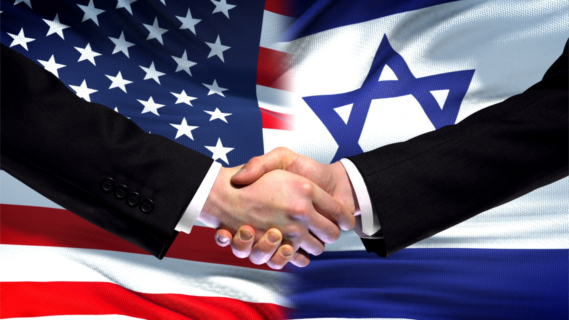 Two hands shaking in front of American and Israeli flags.