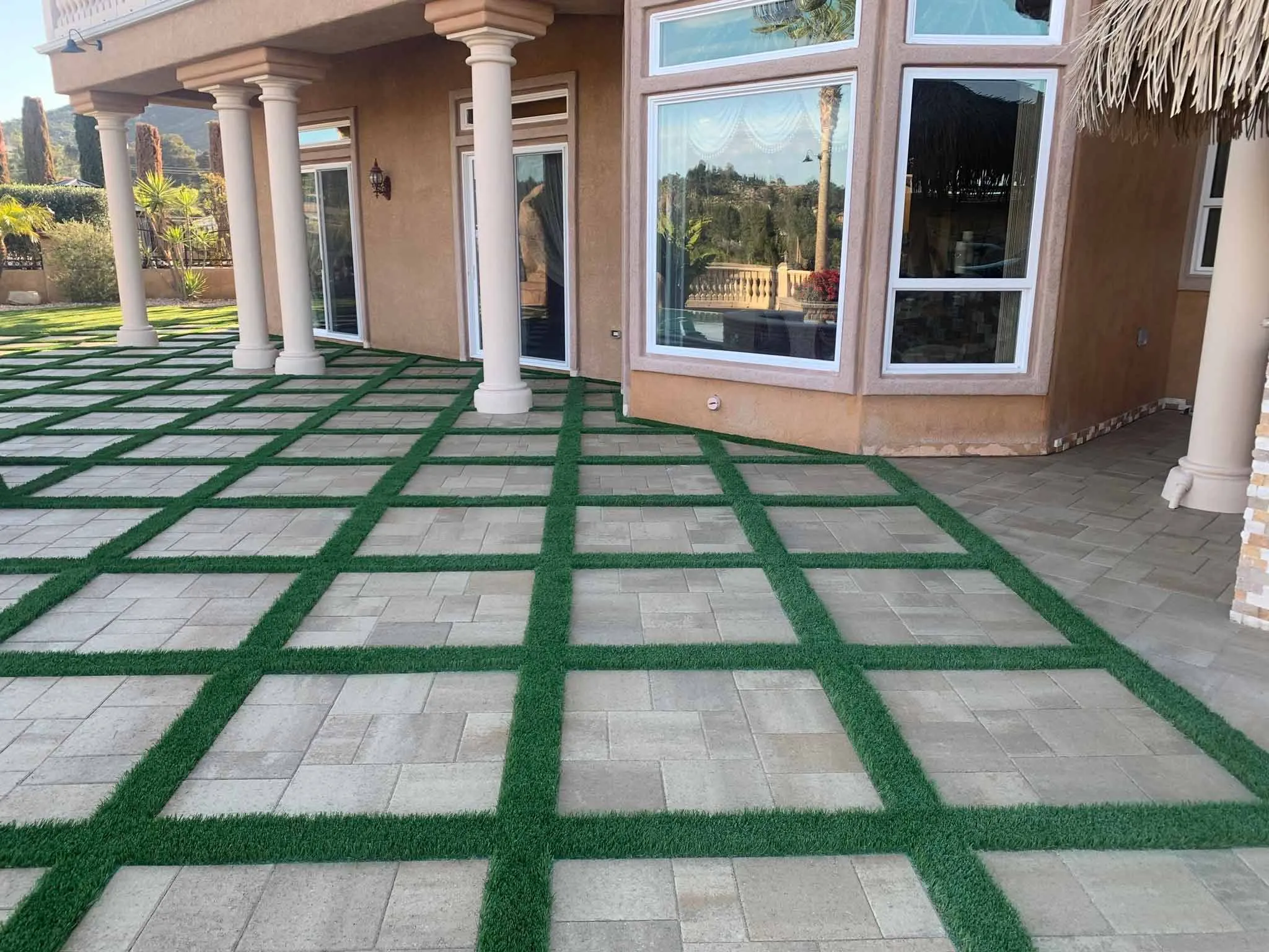 Backyard artificial putting green with three white flags, bordered by mulch and a brick wall.