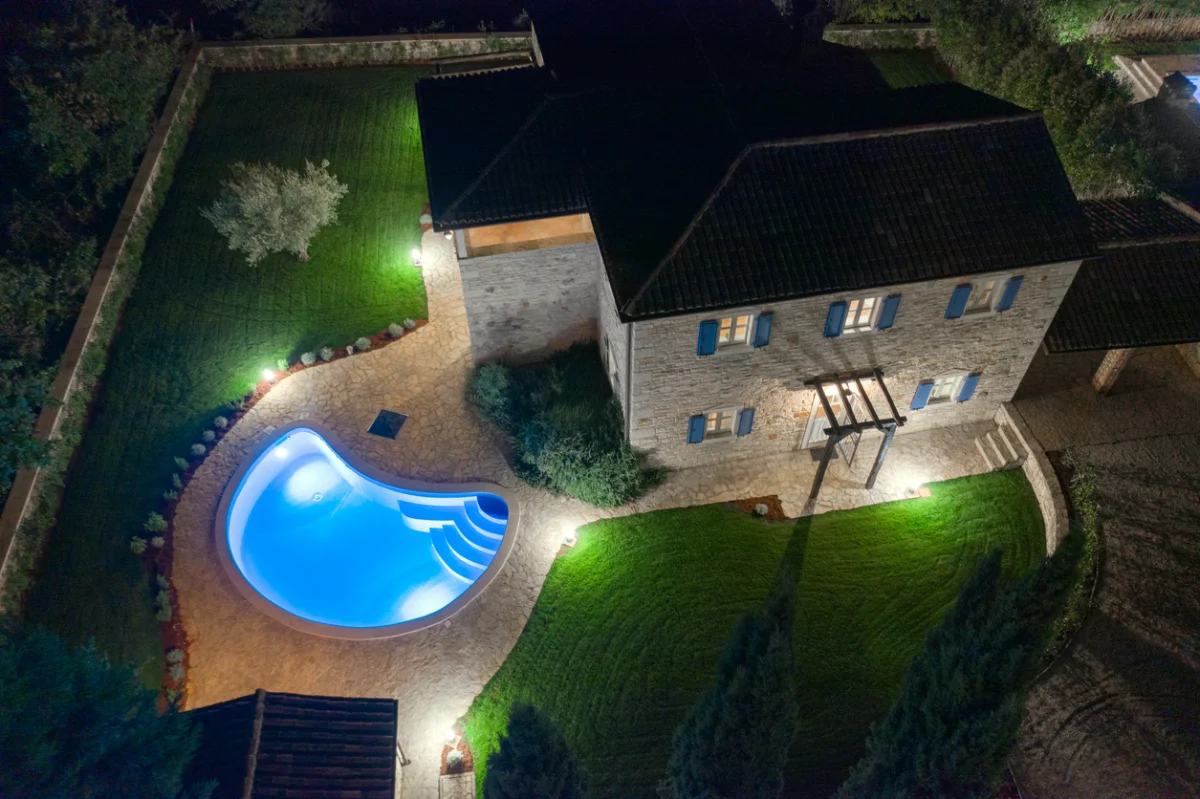Outdoor landscape lighting illuminating a residential home and pool at night
